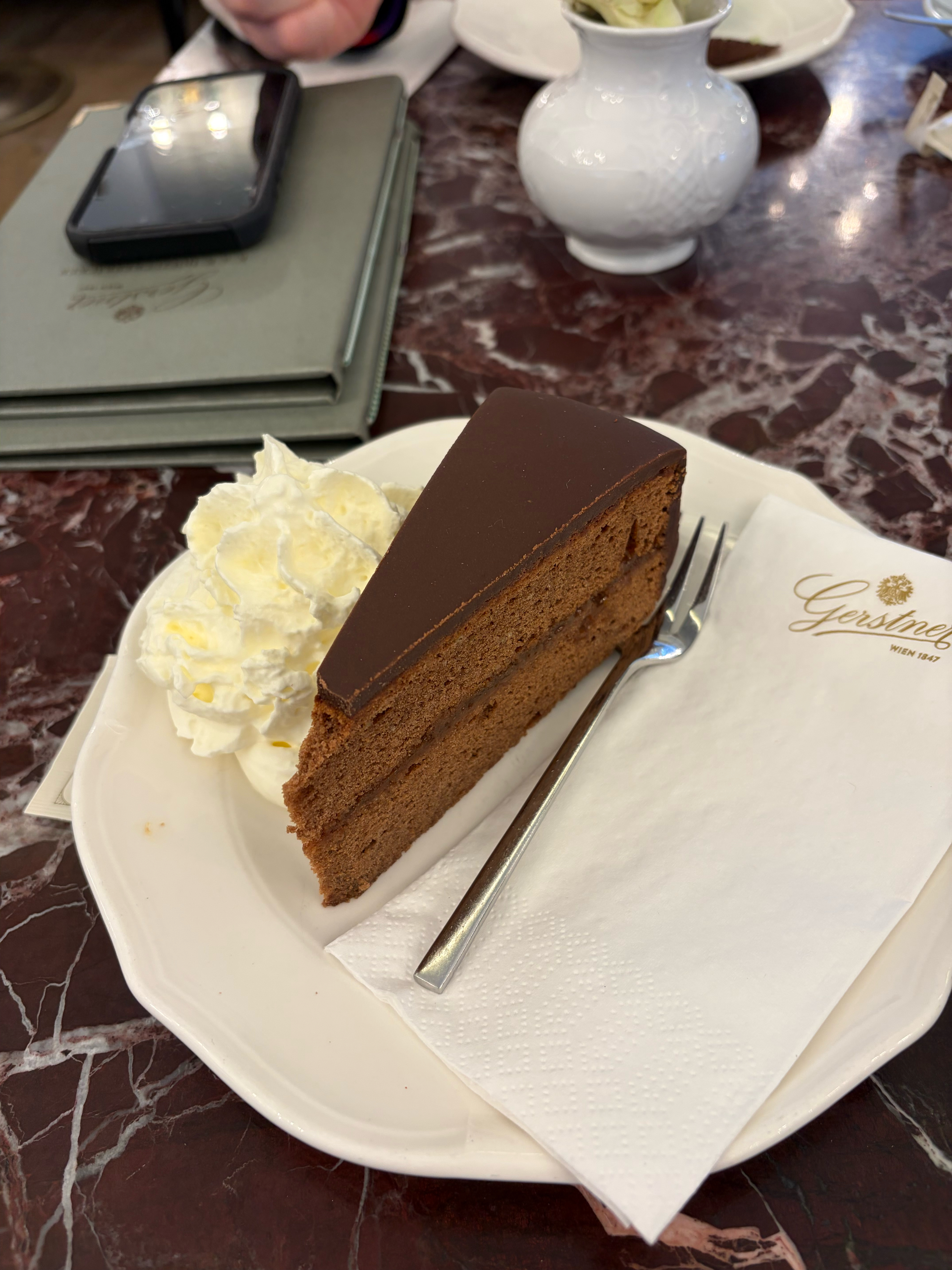 A slice of Sacher Torte with whipped cream on the side